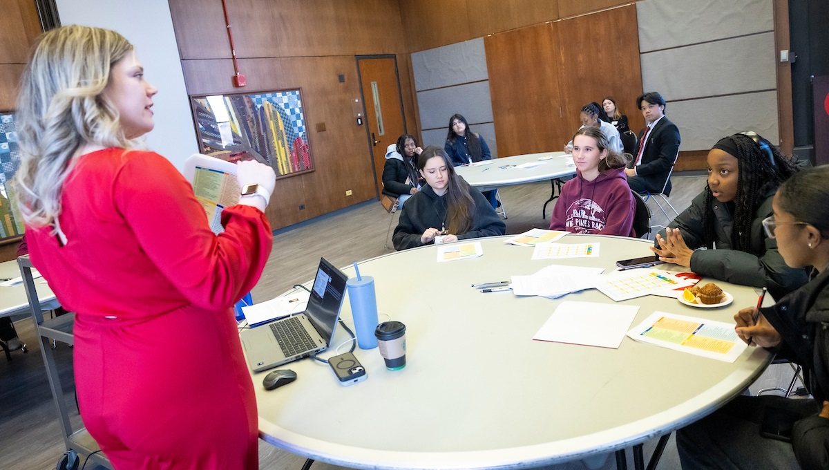 Teenage girls sitting at round tables listening to a woman giving a lecture. Teenage girls sitting at round tables listening to a woman giving a lecture.
